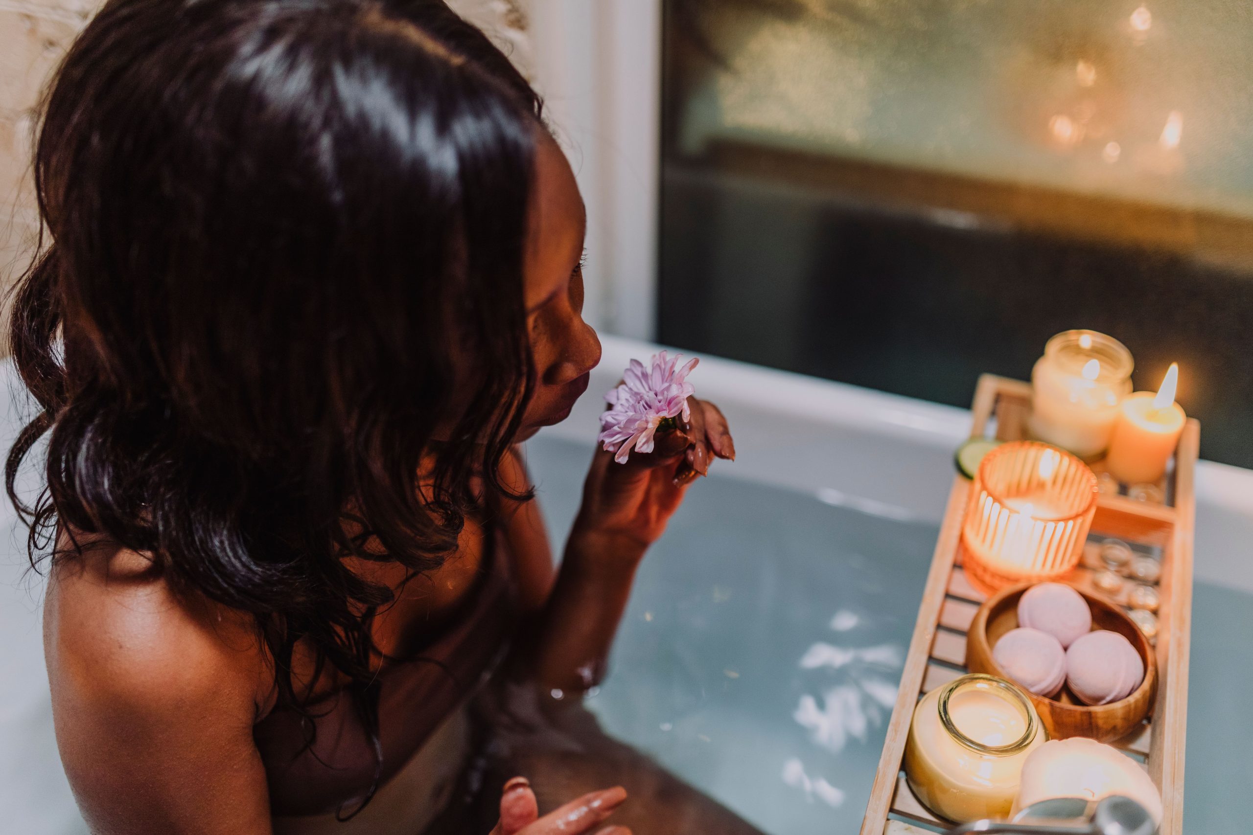 Woman relaxing in a candlelit aromatherapy bath surrounded by flowers