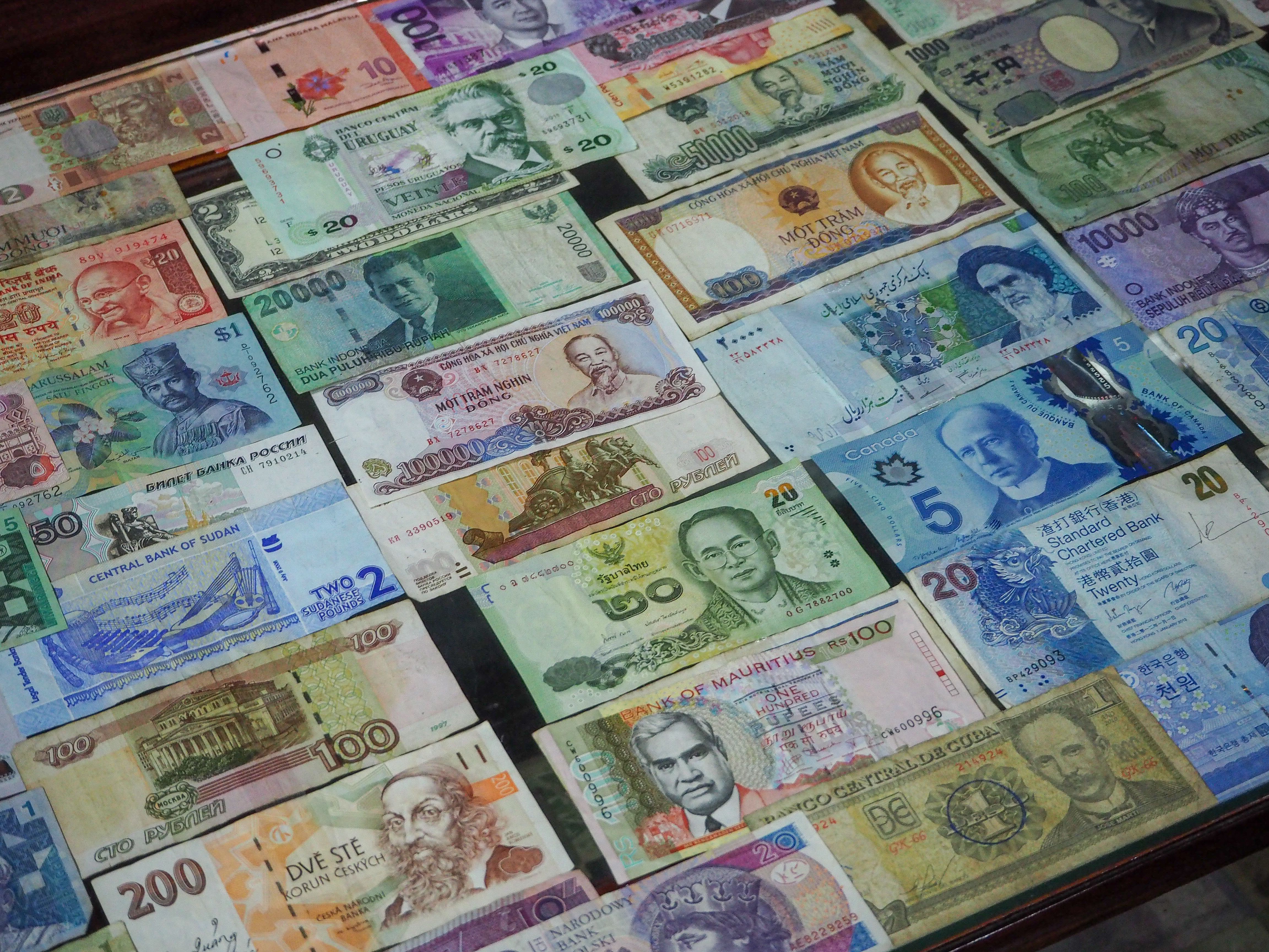 Colorful banknotes from different countries arranged in a row on a table, seen from above.