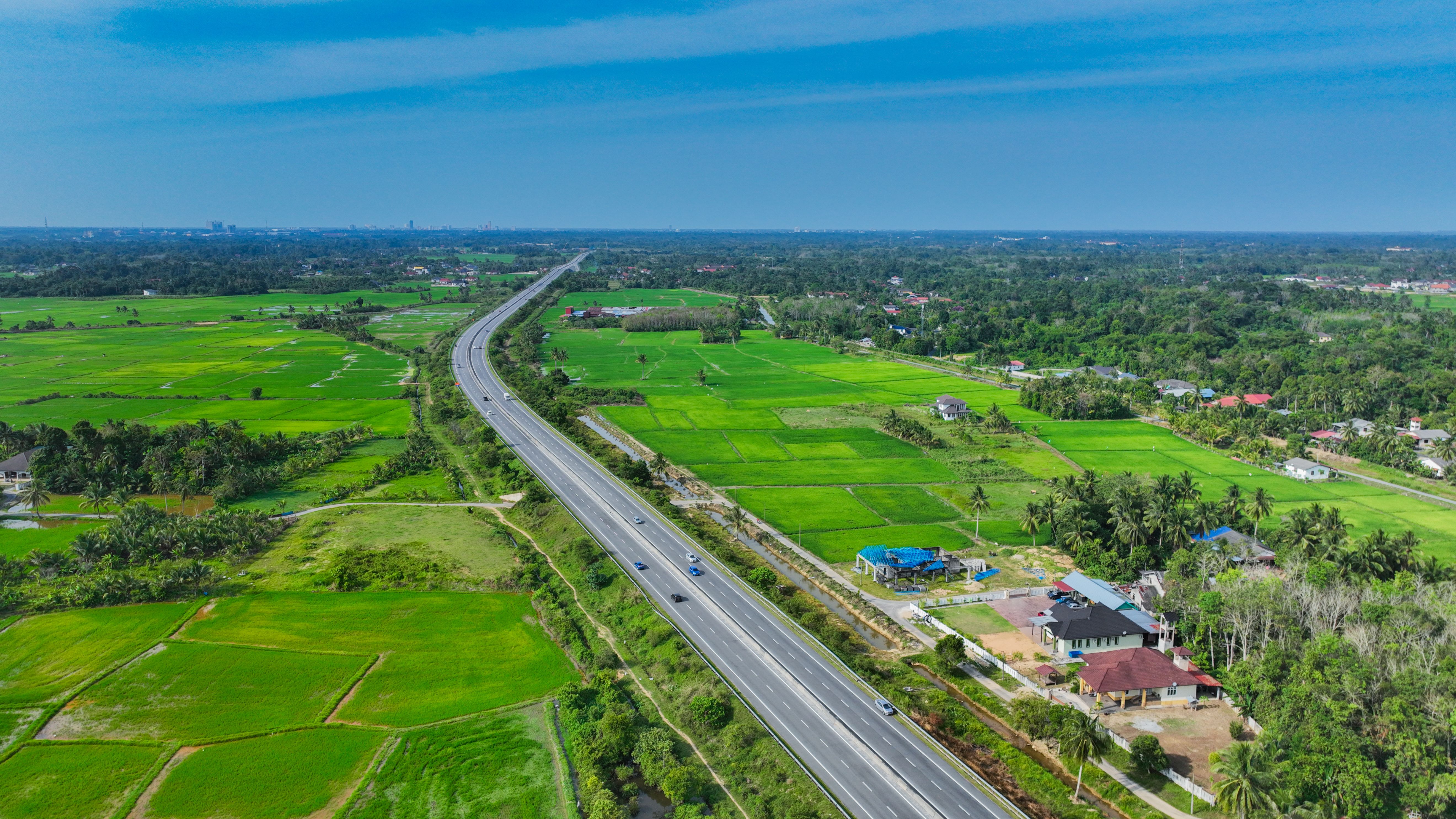 Highway crossing lush rice fields near Kota Bharu, Malaysia, illustrating rural change and connectivity.